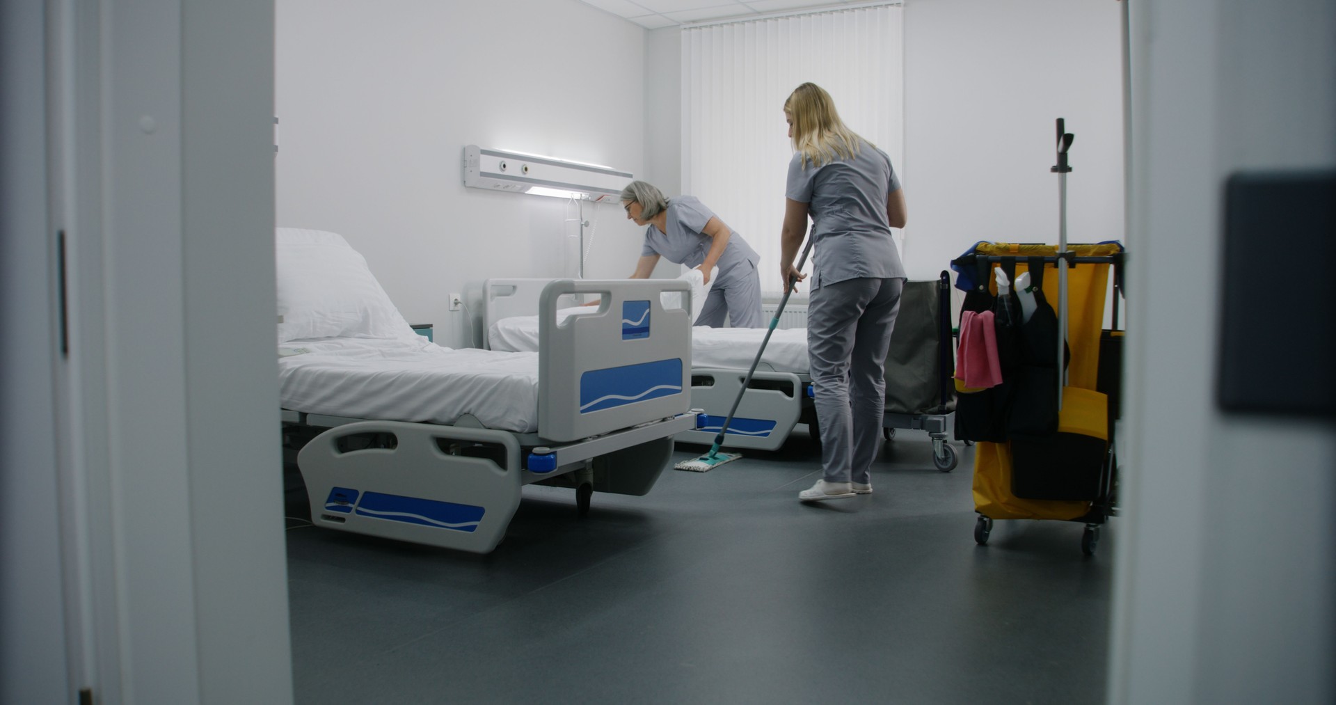 Adult cleaner mops floor with broom in hospital room